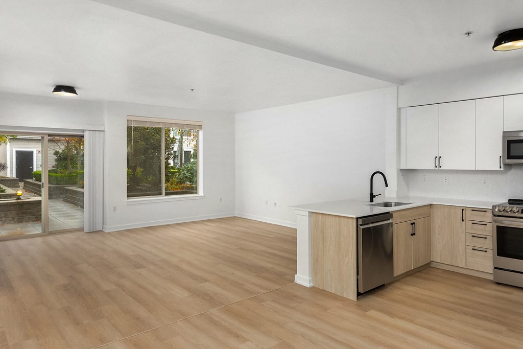 an empty living room with a kitchen and a door to a patio