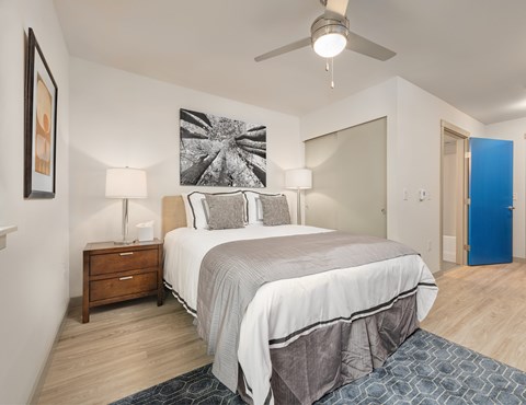 A bedroom with a large bed, a ceiling fan, and a painting on the wall.