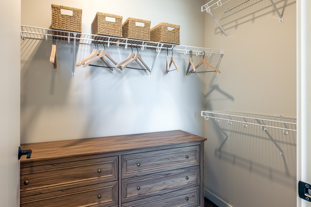 A wooden chest of drawers sits under a metal rack with clothes hanging on it.