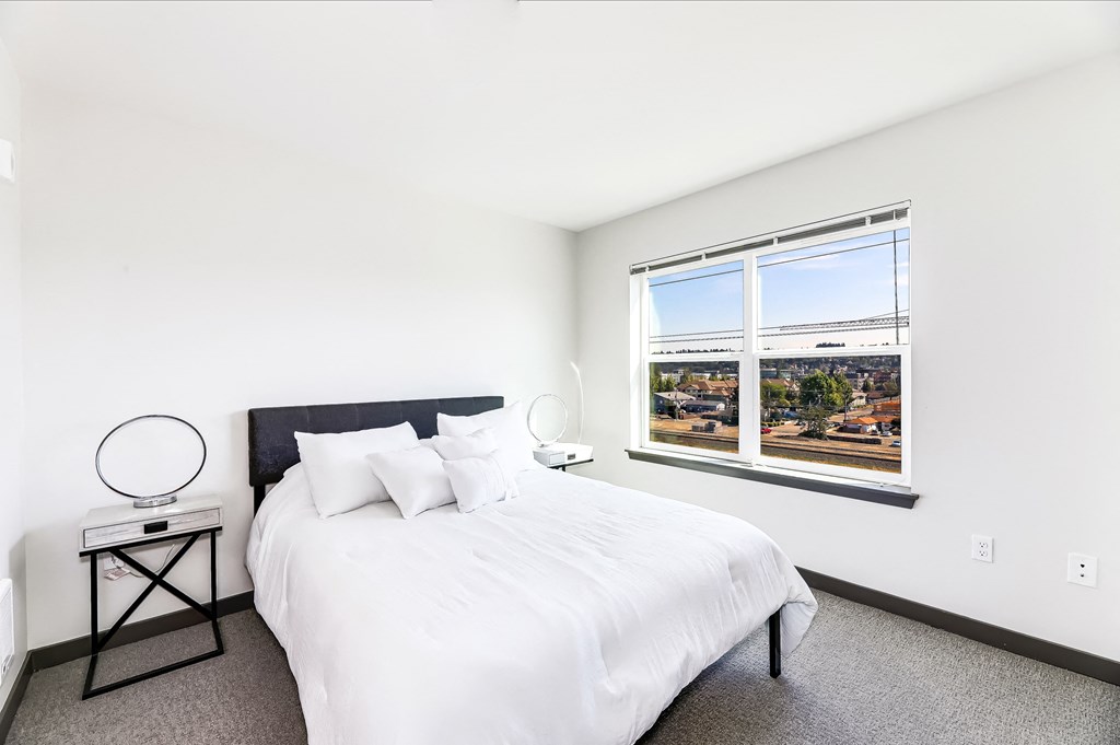 a white bedroom with a large window and a white bed