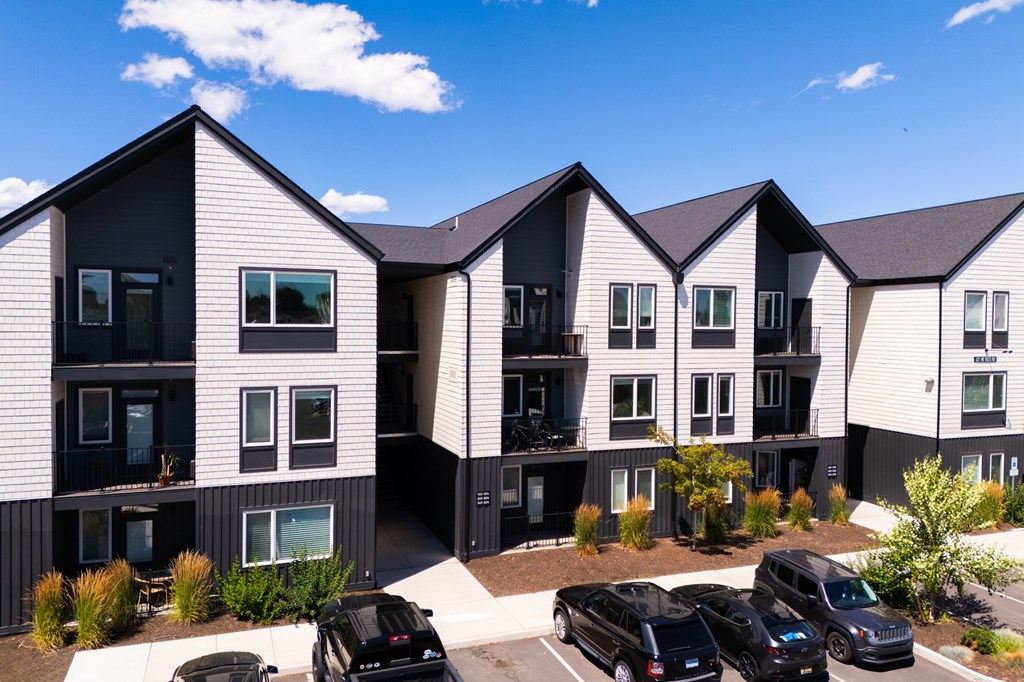 A modern apartment complex with black and white buildings and cars parked in the driveway.