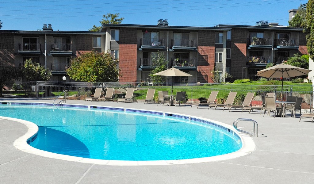 a large pool with chairs and umbrellas in front of an apartment building