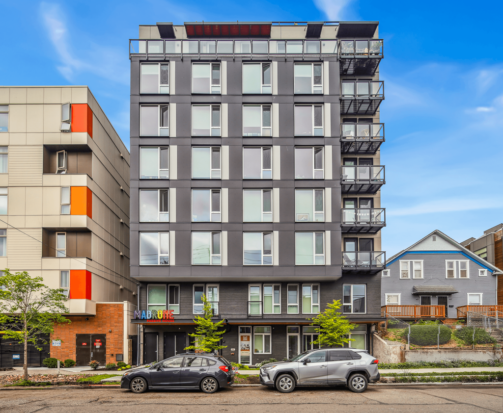 Two cars are parked in front of a modern apartment building.