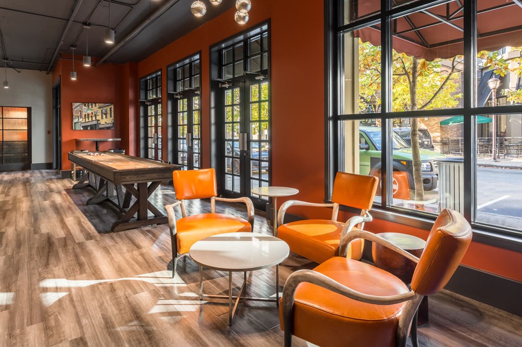 a lounge area with orange chairs and tables and large windows