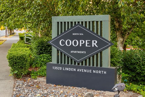 a sign for cooper apartments in front of trees and a sidewalk