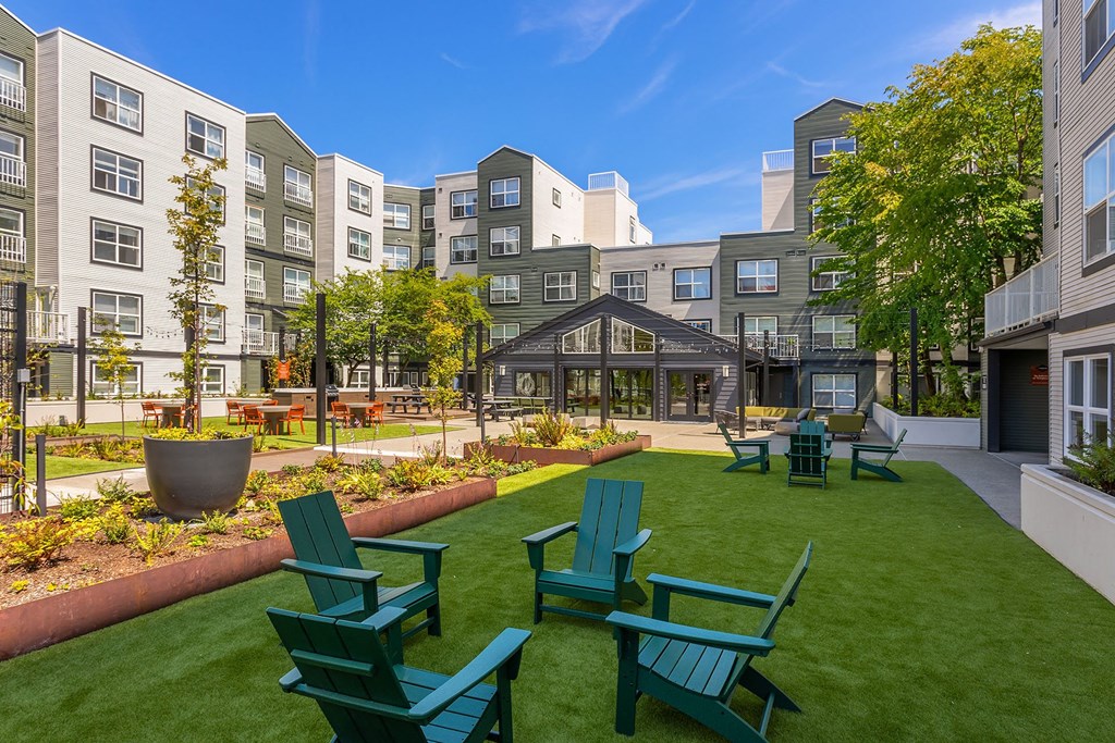 an open courtyard with green grass and chairs in front of apartment buildings