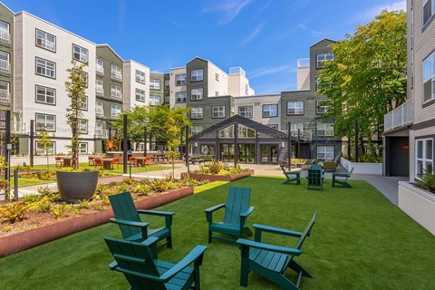 an open courtyard with green grass and chairs in front of apartment buildings