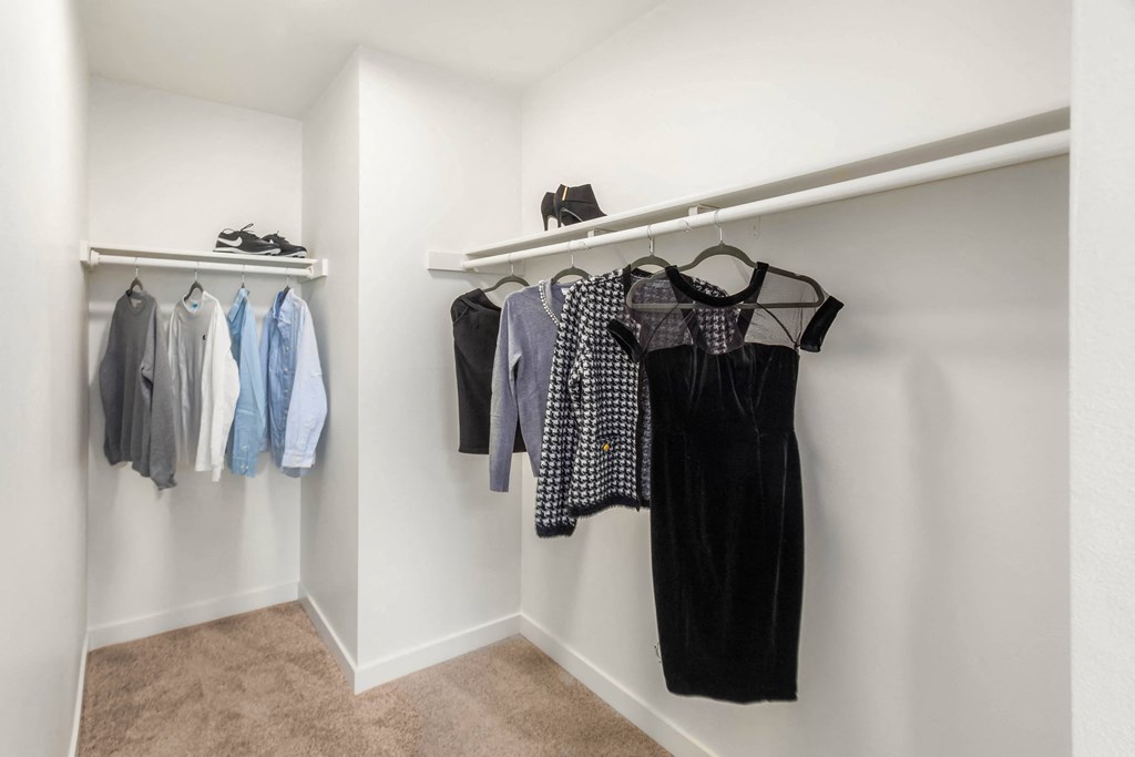 a walk in closet with clothes hanging on a rail and a rack with shoes on