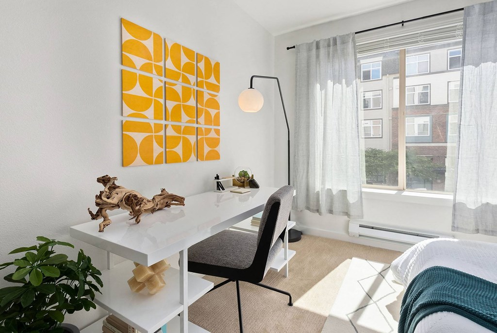 a home office with a desk and a window with a bed