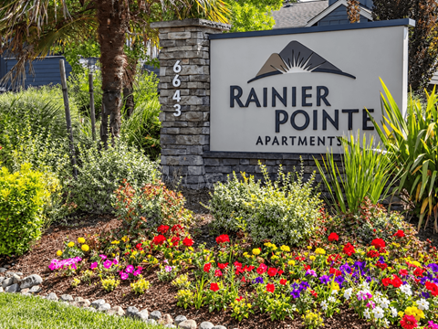 A sign for Rainier Pointe Apartments is surrounded by a colorful flower bed.