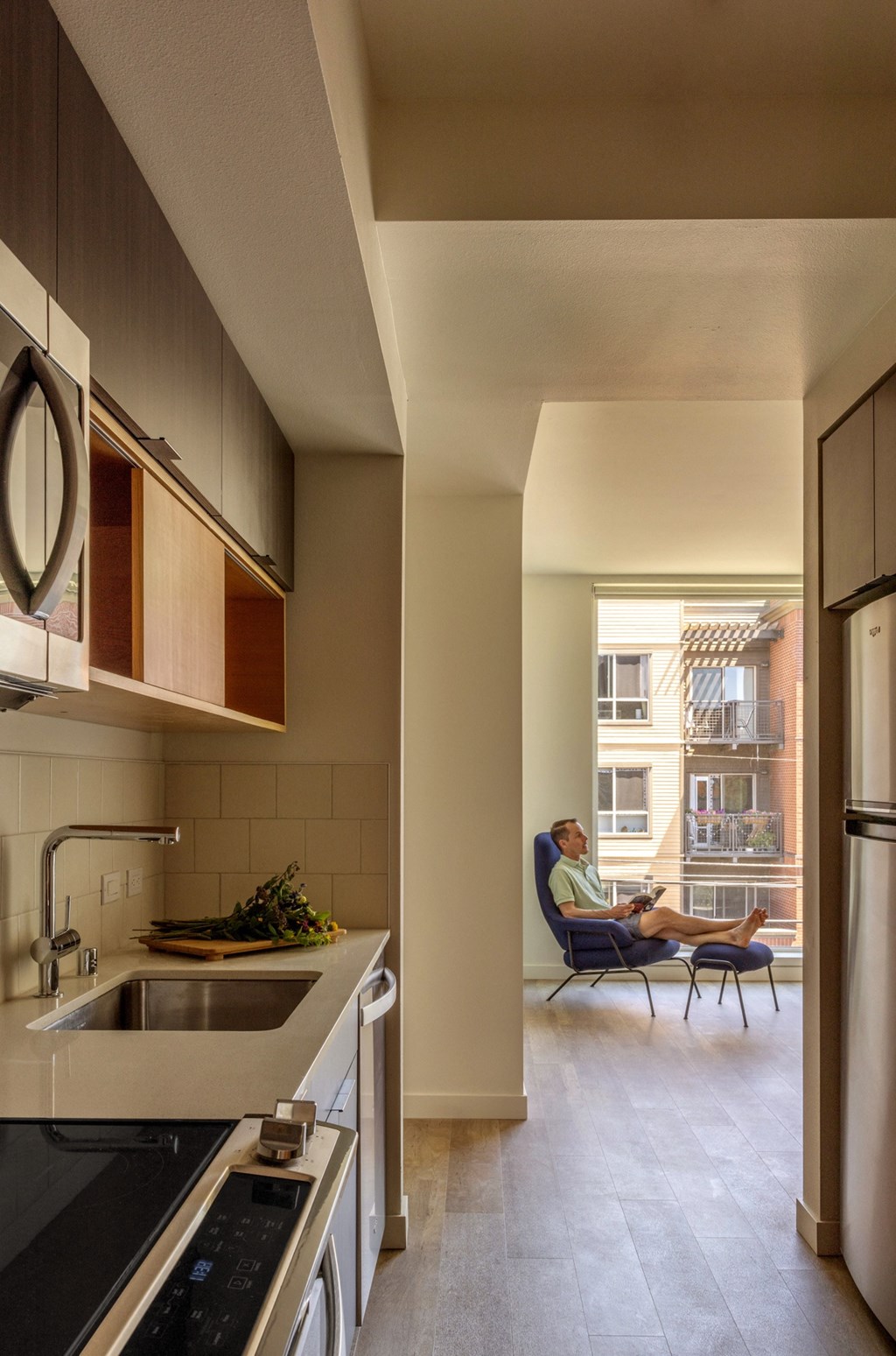 a kitchen and living room with a man sitting in a chair in the window