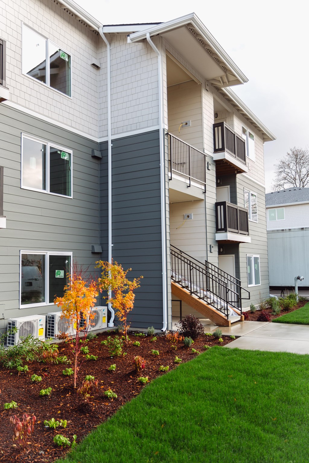 A grey and white apartment building with a tree in front.