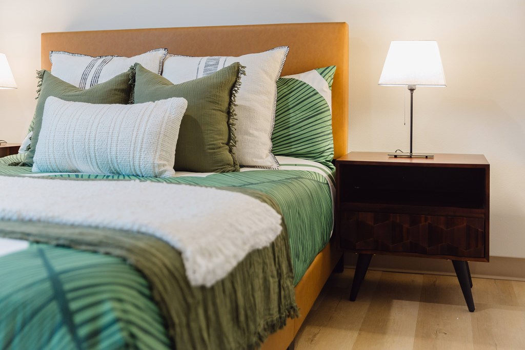 A bed with green and white bedding and a lamp on a side table.
