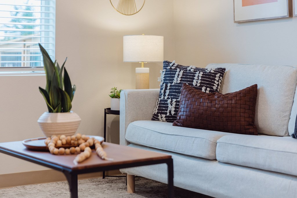 A living room with a white couch, a coffee table with a plant and some decorations on it, and a lamp on a side table.