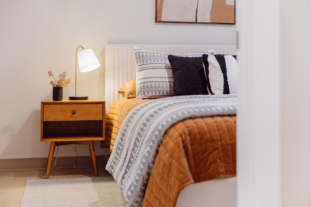 A bedroom with a bed, pillows, a nightstand, and a lamp.