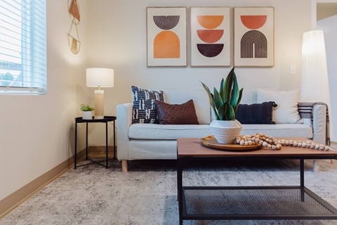 A living room with a couch, a coffee table, and three abstract paintings on the wall.