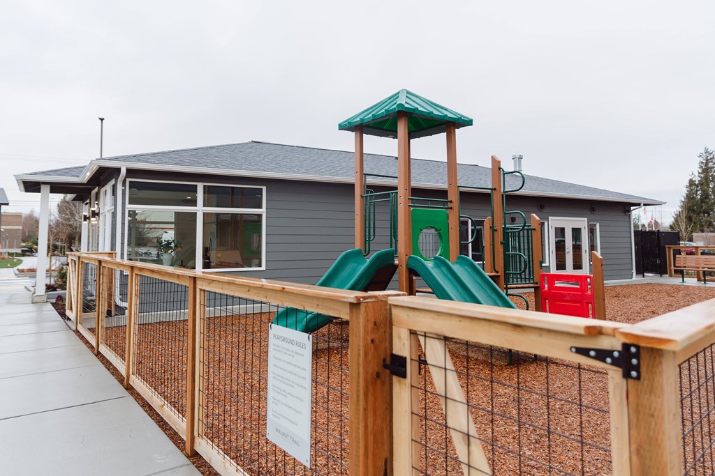 A playground with a green slide and a wooden fence.