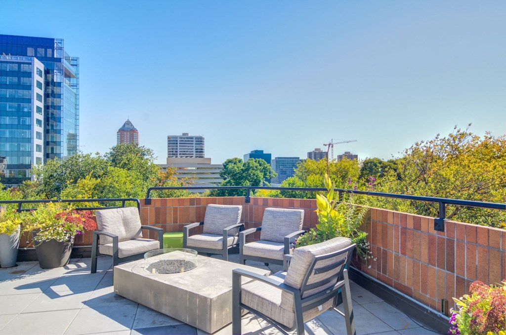 a rooftop patio with chairs and a fire pit and a city in the background