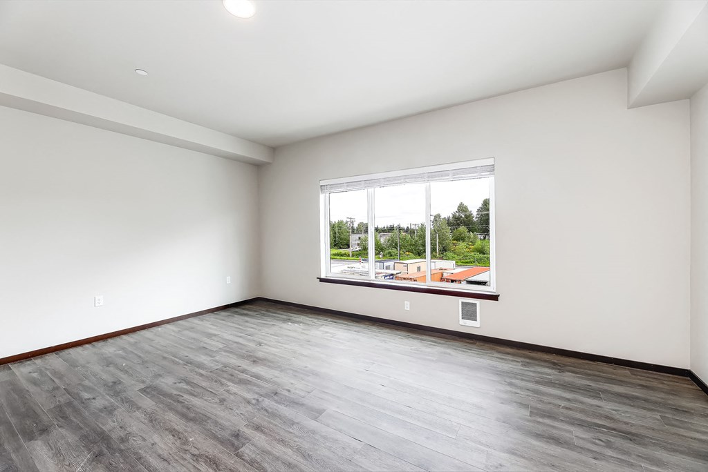 an empty living room with a large window and wood flooring