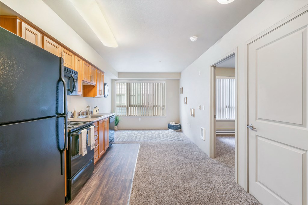 a renovated kitchen with black appliances and wooden cabinets and a door to a living room