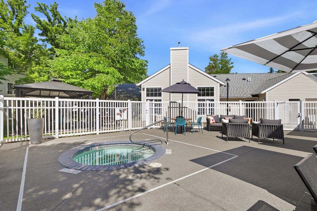 A hot tub is in the middle of a patio with a white fence and a house in the background.