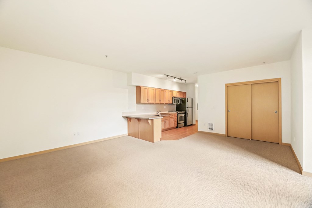 an empty living room and kitchen with wood floors and white walls