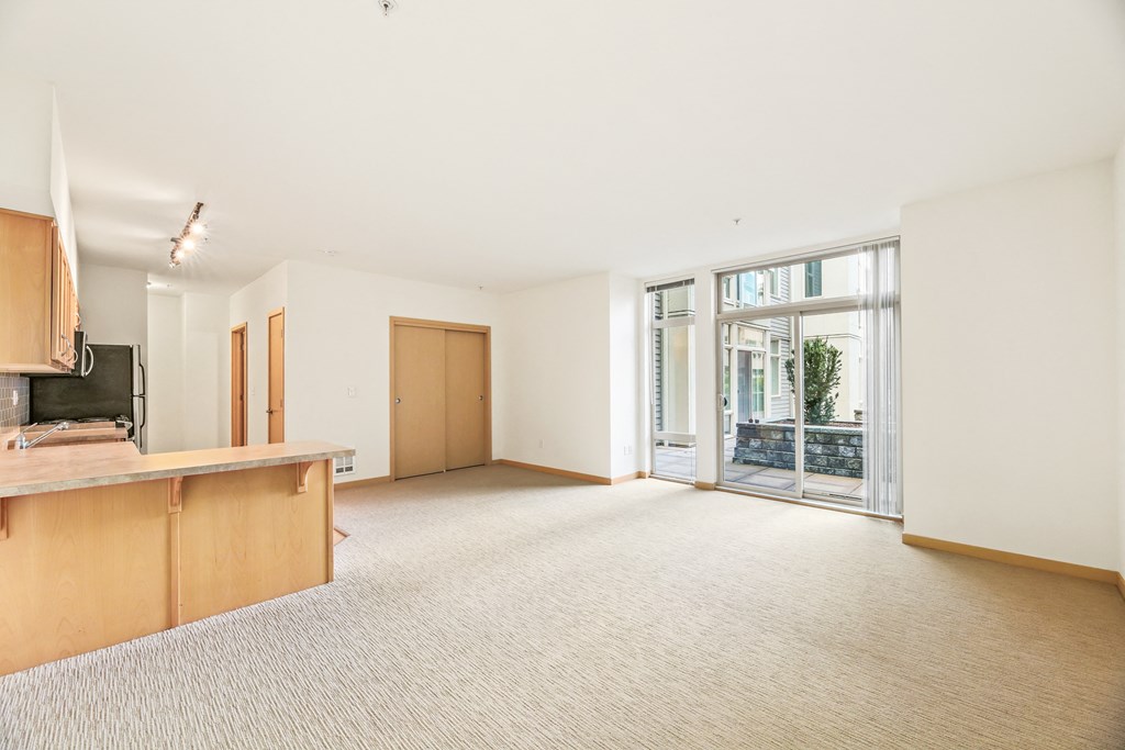 an empty living room with a kitchen and a balcony