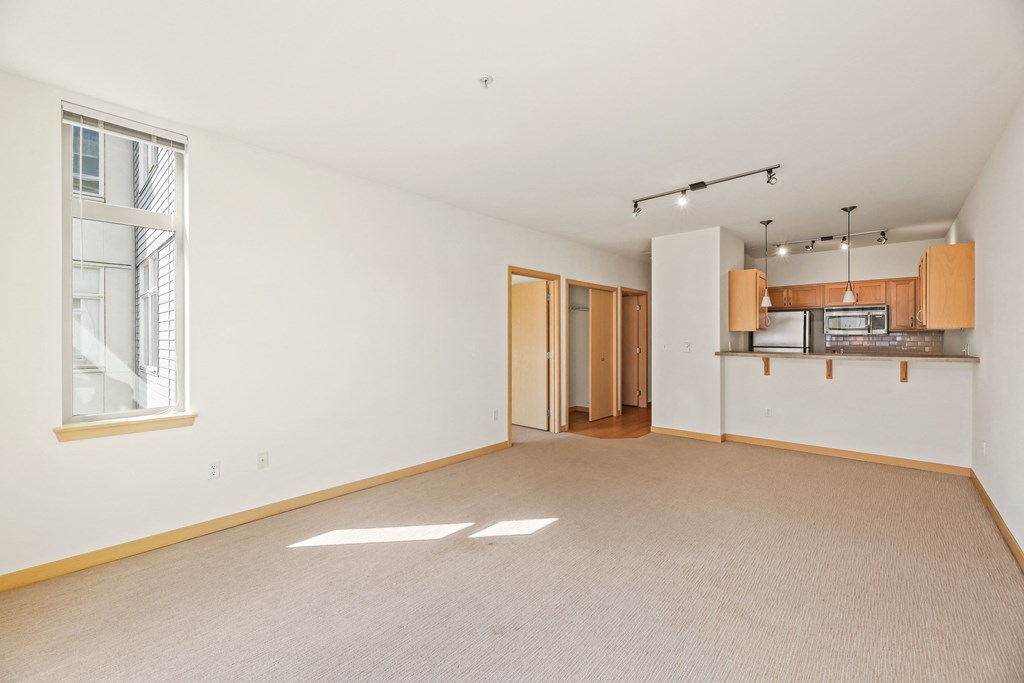 an empty living room with a kitchen and a window