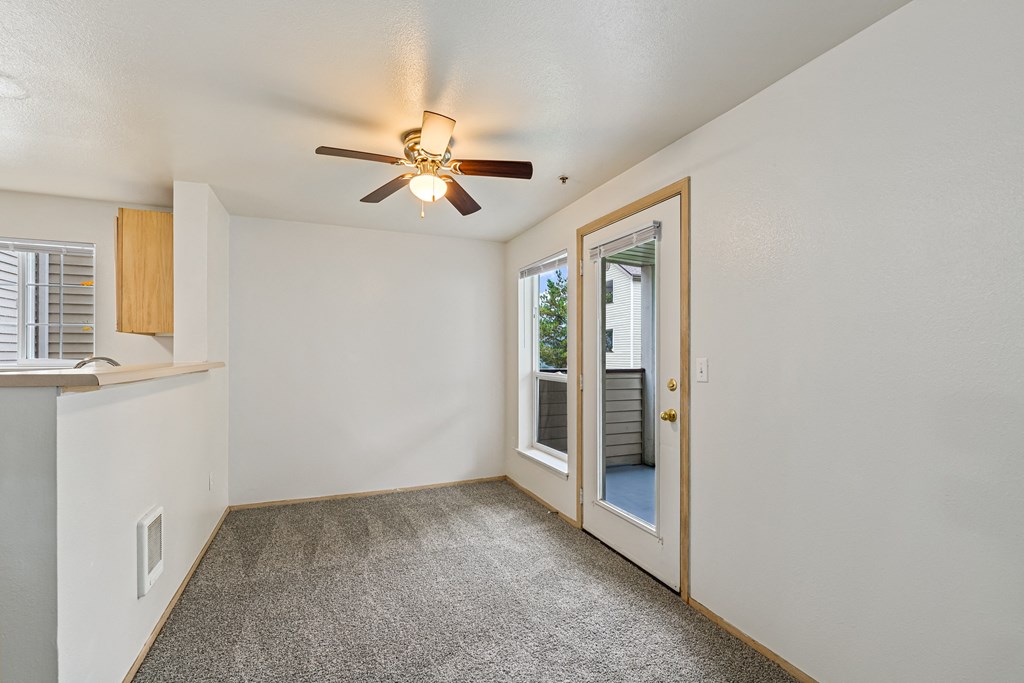 an empty living room with a ceiling fan and a door to a balcony