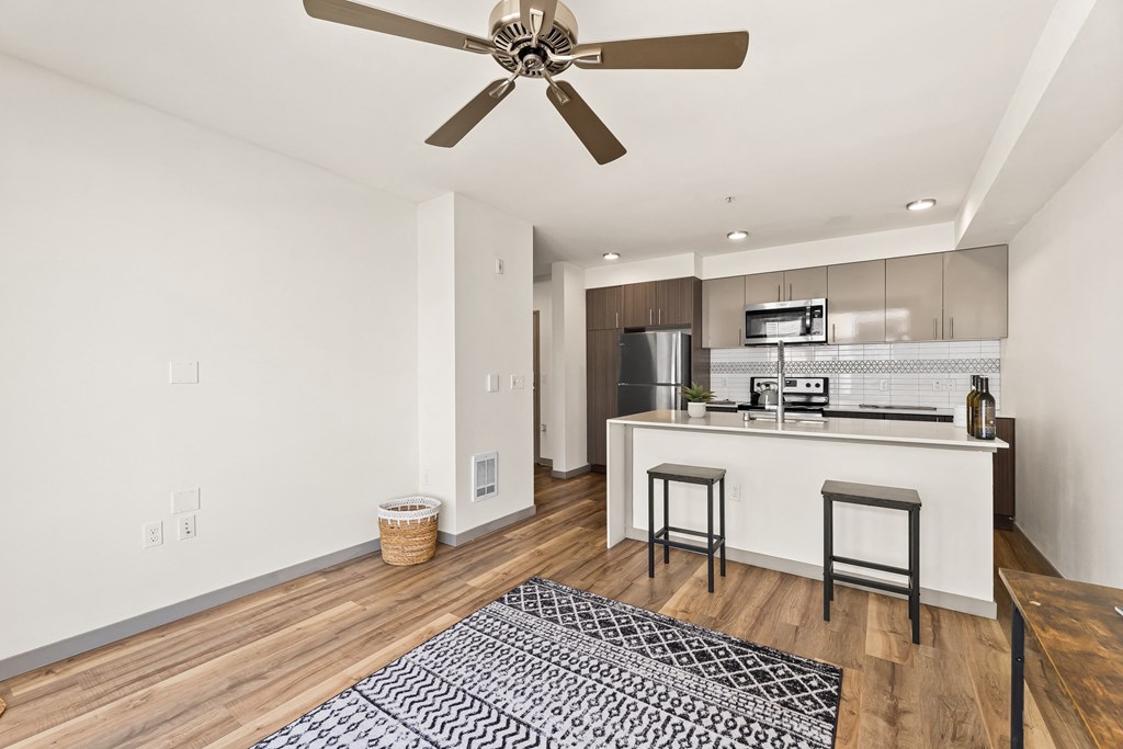 a living room and kitchen area with a ceiling fan and hardwood floors