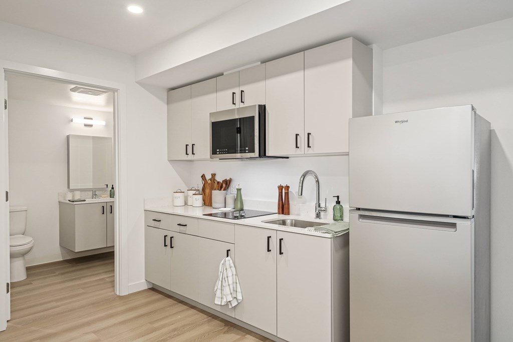 A white kitchen with a refrigerator, sink, and cabinets.