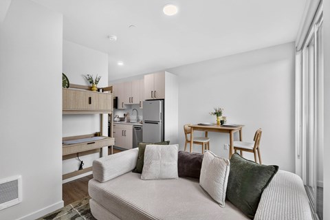 A well-lit, modern living room with a couch, a dining table, and a kitchen area in the background.