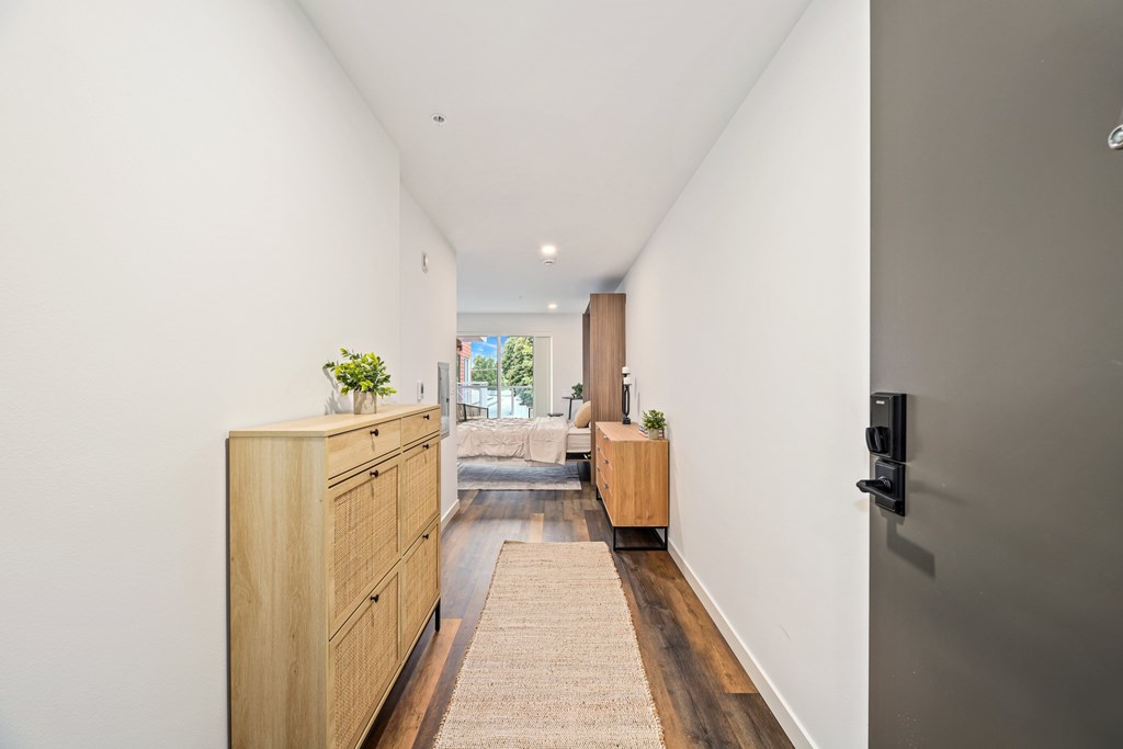 A long hallway with a tan carpet and a wooden cabinet on the left.