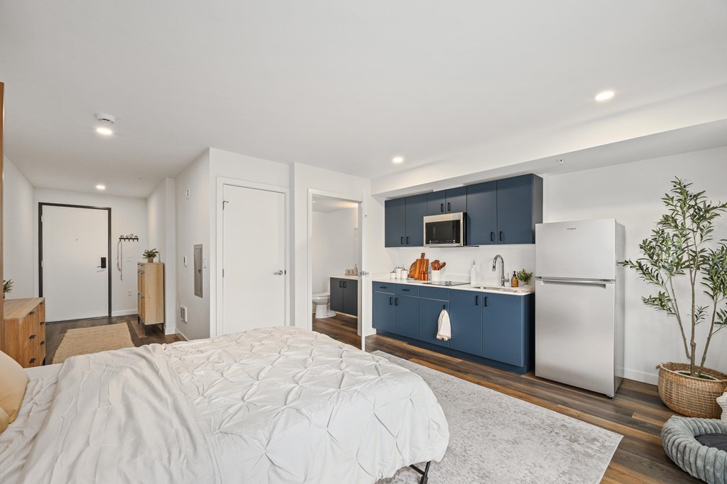 A bedroom with a large bed and a kitchen area in the background.