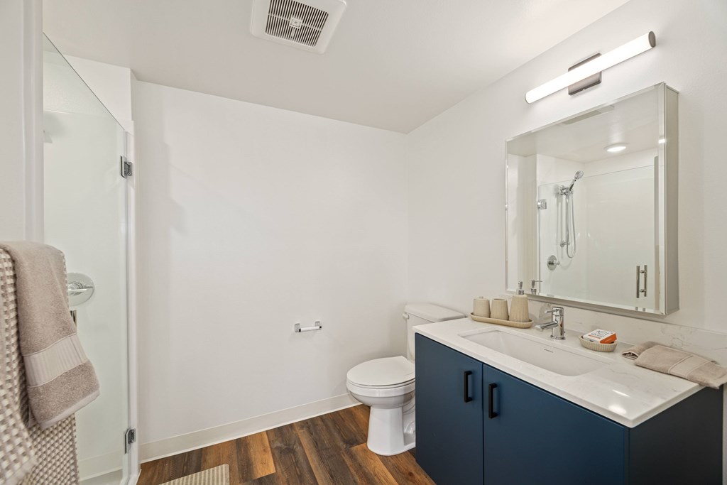 A bathroom with a toilet, sink, mirror, and a towel hanging on the door.