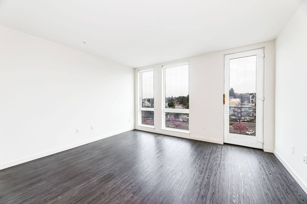 an empty living room with wood floors and large windows