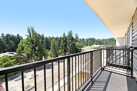 A balcony with a metal railing overlooks a street and trees.
