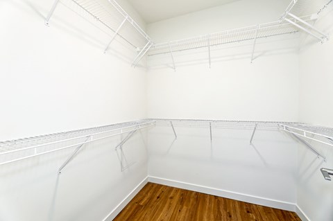 Empty walk-in closet with white walls and wooden floor.