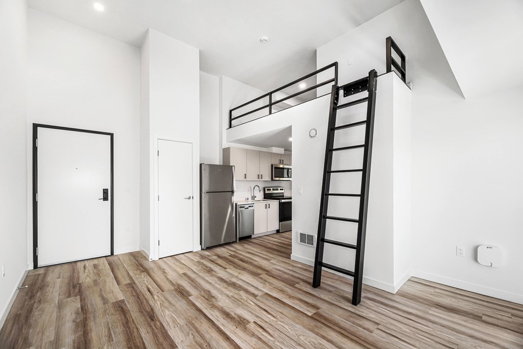 A black ladder is leaning against a wall in a white room with wood flooring.