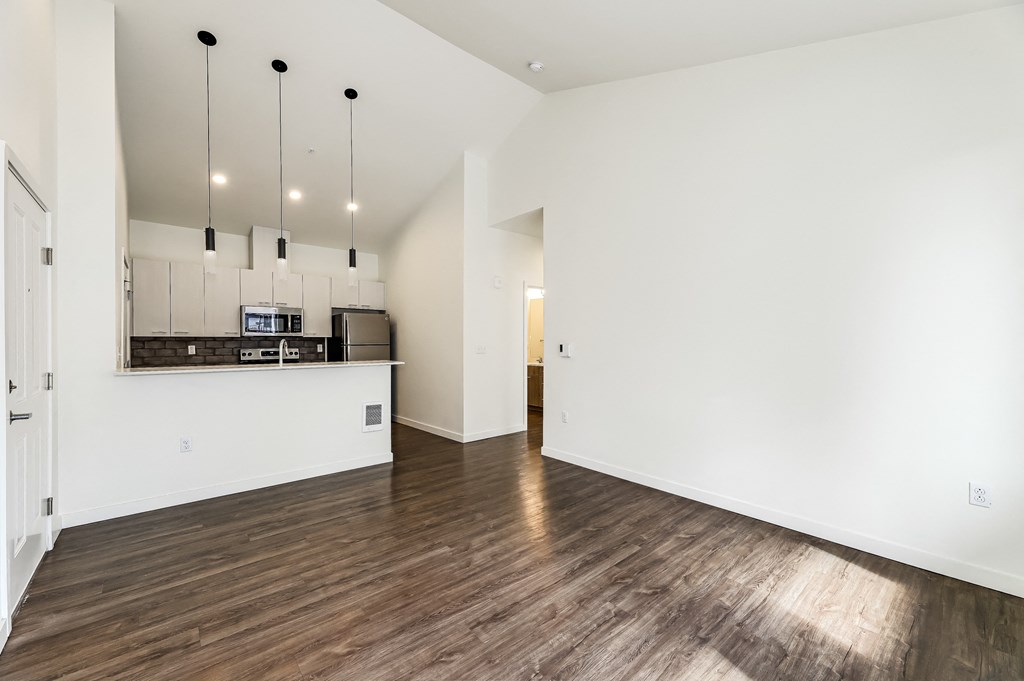 a living room and kitchen with white walls and wood floors