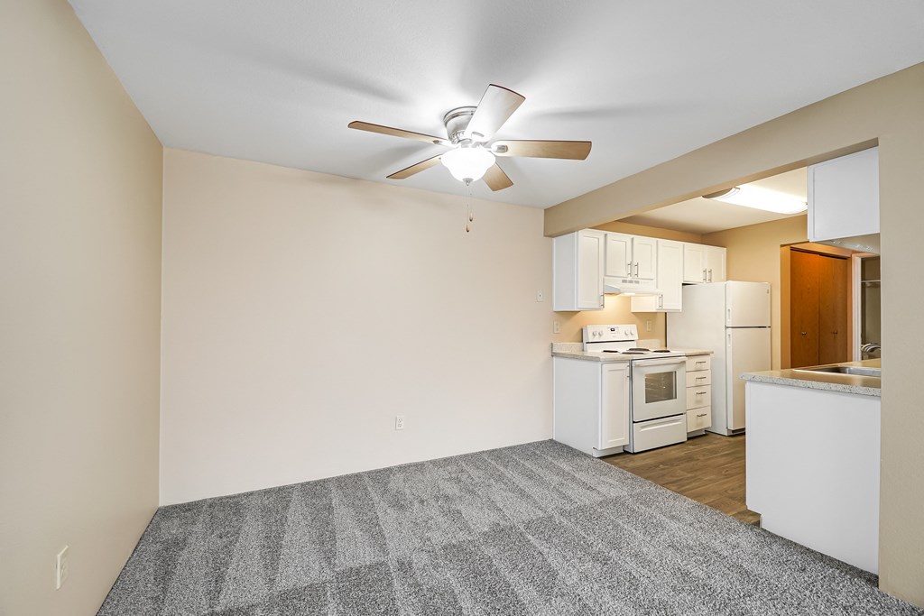 an empty living room with a kitchen and a ceiling fan