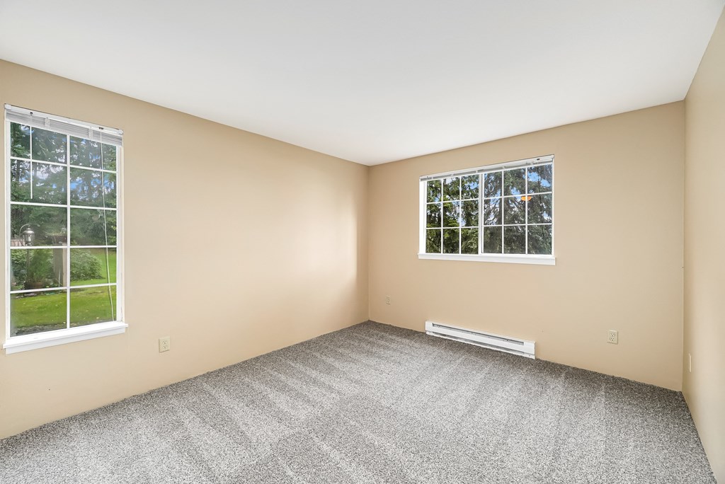 an empty room with two windows and carpeting