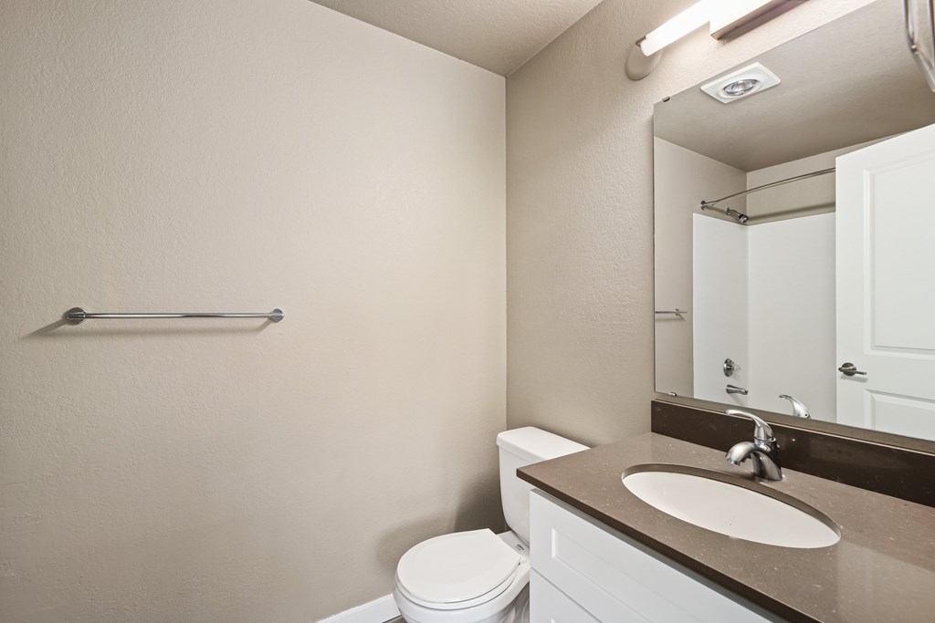 A bathroom with a toilet, sink, mirror, and towel rack.