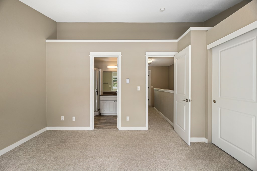 A room with beige walls and carpeting, with a white door on the right and a white cabinet with a mirror in the center.