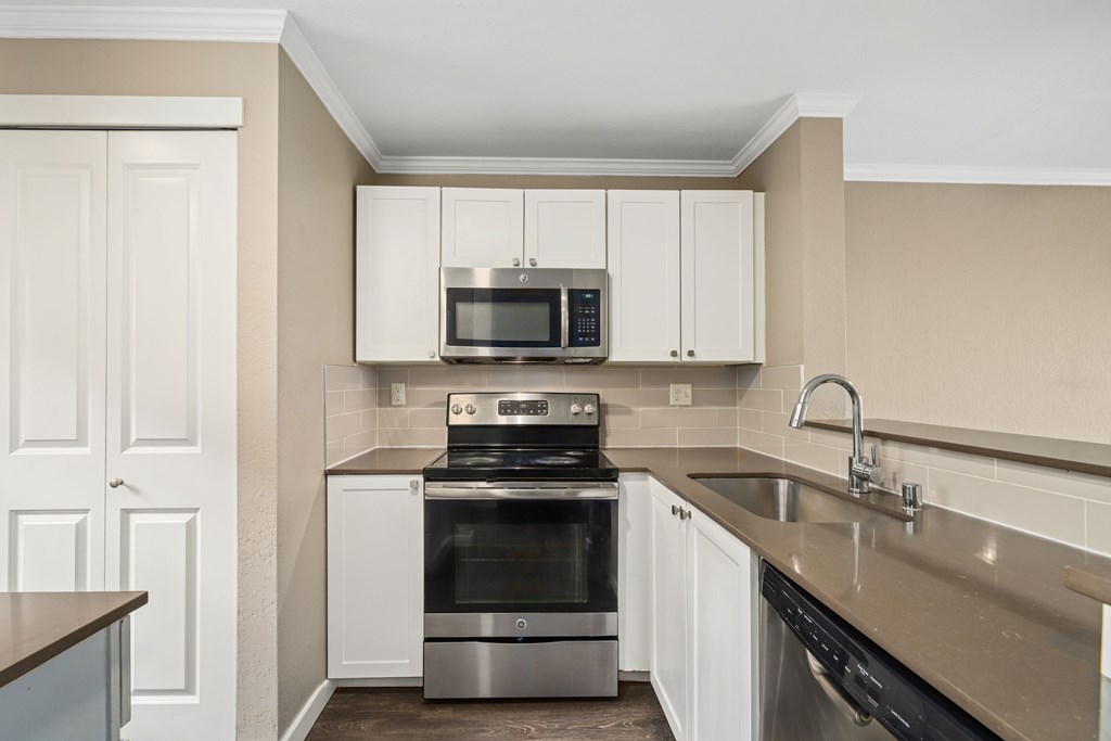 A kitchen with a stove, oven, microwave, and cabinets.