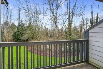 A view from a balcony overlooking a green lawn and trees.