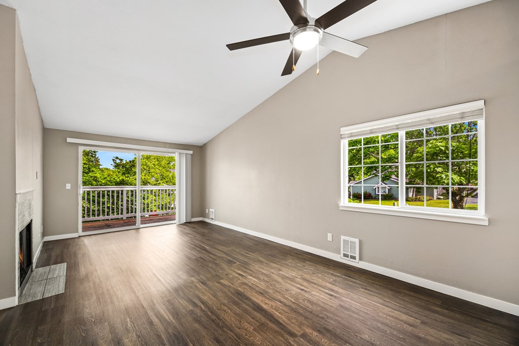 A room with a ceiling fan and a window overlooking a green area.