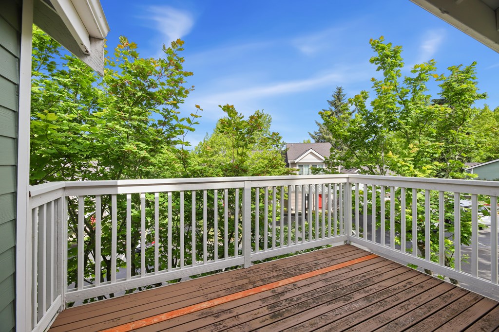 A wooden deck with a white railing and trees in the background.