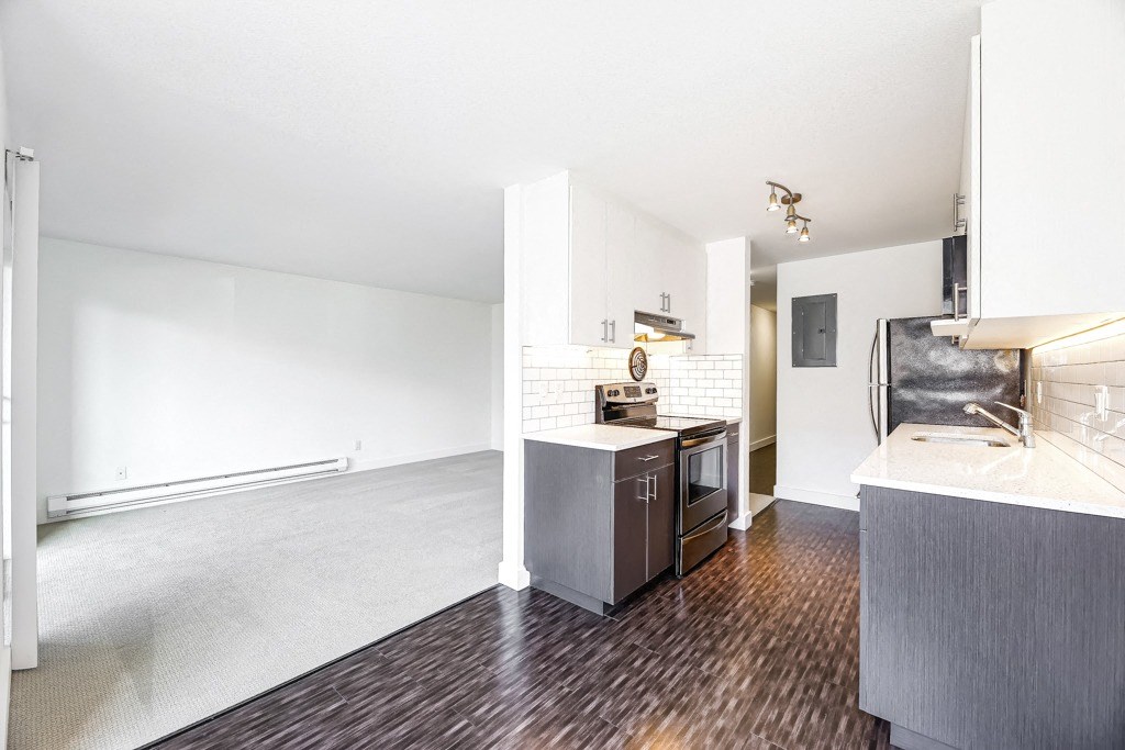 an empty living room and kitchen with wood flooring and white walls