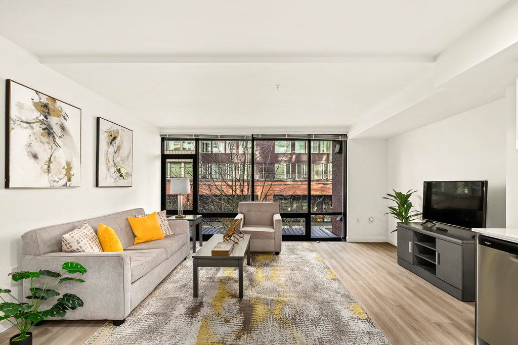 A living room with a grey couch, a coffee table, a television, and a large window.